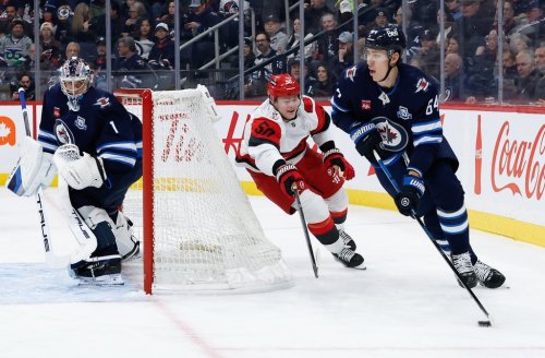 Carolina Hurricanes' Eric Robinson (50) chases Winnipeg Jets' Logan Stanley (64) as goaltender Eric Comrie (1) looks on during first period NHL action in Winnipeg on Friday, November 21, 2025. THE CANADIAN PRESS/John Woods