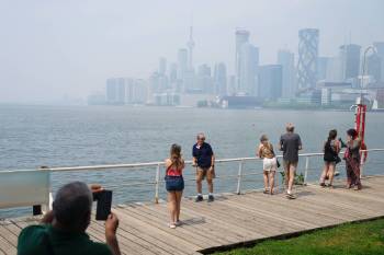 Tourists pose for a photo against a city view of Toronto on July 14 as the Air Quality Health Index rating soared to over 10, or “very high risk,” from wildfire smoke. (The Canadian Press files)