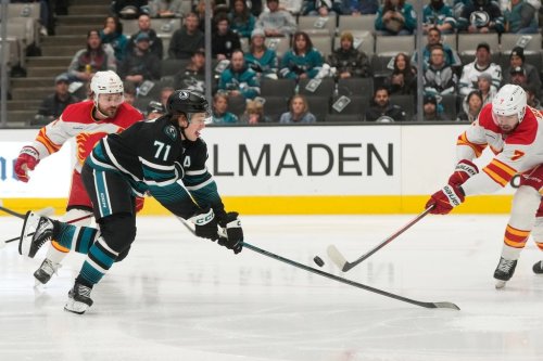 San Jose Sharks centre Macklin Celebrini (71) reaches for the puck against Calgary Flames defenceman Rasmus Andersson, left, and defenceman Kevin Bahl (7) during the first period of an NHL hockey game in San Jose, Calif., Tuesday, Dec. 16, 2025. (AP Photo/Jeff Chiu)