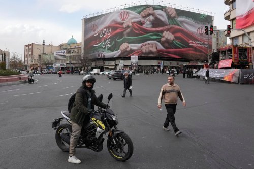 A man stands with his motorbike in front of a huge banner showing hands holding Iranian flags as a sign of patriotism, in Tehran, Iran, Wednesday, Jan. 14, 2026. (AP Photo/Vahid Salemi)