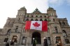 A gigantic Canadian flag hangs over the ceremonial entrance at the legislature as people walk about in Victoria, B.C., on Friday, March 7, 2025. THE CANADIAN PRESS/Chad Hipolito