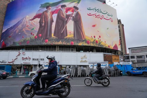 Motorbikes drive past a billboard depicting Iran’s late Supreme Leader Ayatollah Ali Khamenei, centre, handing the country’s flag to his son and successor Ayatollah Mojtaba Khamenei, right, as the late revolutionary founder Ayatollah Ruhollah Khomeini stands at left, in a square in downtown Tehran, Iran, Tuesday, March 10, 2026. (AP Photo/Vahid Salemi)