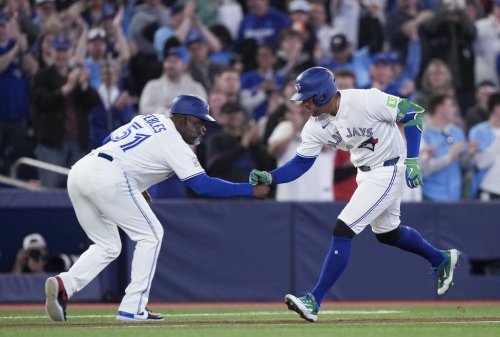 Blue Jays designated hitter George Springer (4) celebrates his solo home run with third-base coach Carlos Febles (51) in a Major League Baseball game against the Athletics in Toronto on March 29, 2026. THE CANADIAN PRESS/Nathan Denette