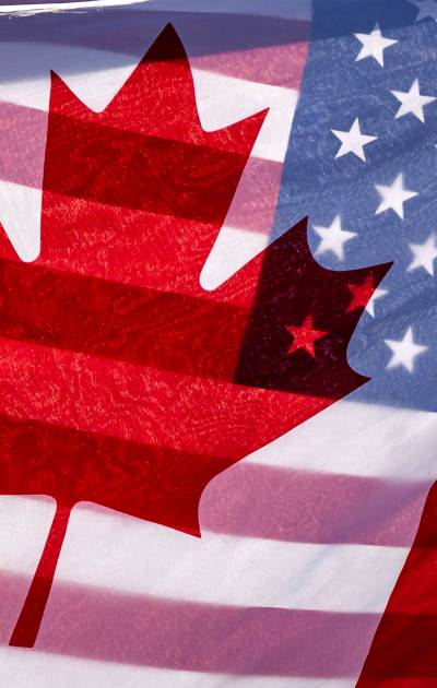 Sunlight shines through the flags of Canada and the United States, held together by a protester outside on Parliament Hill in Ottawa, in February 2025. A new poll highlights a major difference between Canadians and Americans. (The Canadian Press)