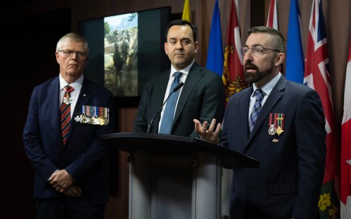 Former chief of defence staff Rick Hillier (left) and Conservative MP for Airdrie-Cochrane Blake Richards look on as Valour in the Presence of the Enemy founder Bruce Moncur speaks during a news conference on Parliament Hill in Ottawa on Wednesday, April 15, 2026. THE CANADIAN PRESS/Adrian Wyld