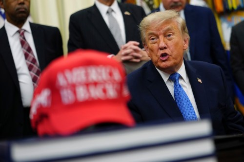 President Donald Trump speaks alongside a red cap stating 