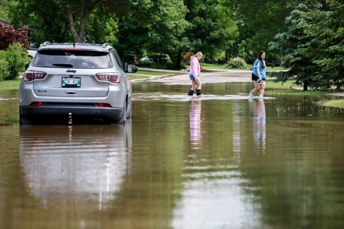 People walk by a flooded and abandoned vehicle on Alan McLeod Ave. in Stonewall, Man., on Wednesday, June 10, 2026. THE CANADIAN PRESS/John Woods
