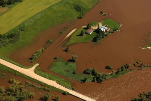 A home and farm sit on an island of dry land, surrounded by the floodwaters of the swollen Assiniboine River just west of Russell in early July. Russell is included in an overland flood watch issued by the province on Friday. (Tim Smith/The Brandon Sun)
