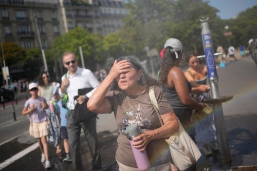 Tourists enjoy cooling off at a public water fountain In Paris, Friday, June 26, 2026. (AP Photo/Christophe Ena )