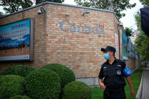 In this Aug. 6, 2020 photo, a security officer wearing a face mask stands outside the Canadian Embassy in Beijing, China. (AP Photo/Mark Schiefelbein, File)
