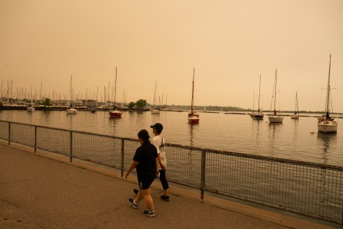 People walk on the waterfront in Toronto as wildfire smoke fills the city on Wednesday. (The Canadian Press)