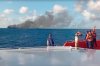 In this image made from video released by the Indonesian National Search and Rescue Agency (BASARNAS), the crew of a rescue ship look on as smoke billows from a passenger ferry that caught fire while traveling from the tourist island of Bali to neighboring island of Lombok, in the waters of Lombok Strait, Indonesia, Wednesday, Aug. 12, 2026. (BASARNAS via AP)