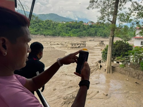 People take photographs and videos of the swollen, debris-choked banks of the Trishuli River after a flash floods in Nepal's Nuwakot district on Wednesday, Aug. 26, 2026. (AP Photo/Niranjan Shrestha)