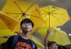 FILE - Hong Kong teenage student leader Joshua Wong, left, stands in front of yellow umbrellas outside a magistrates' court in Hong Kong, on Sept. 2, 2015. (AP Photo/Vincent Yu, File)