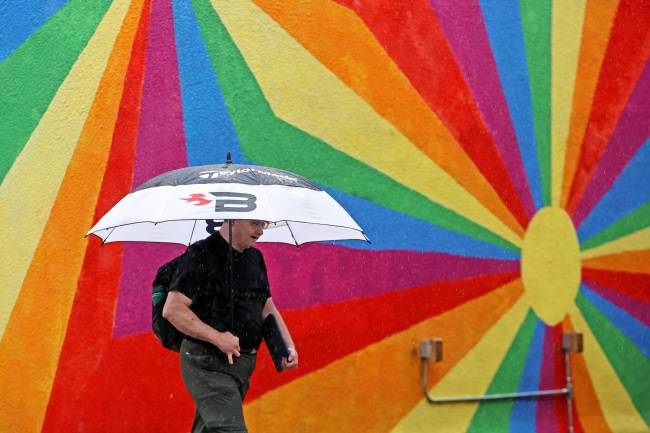 An umbrella-wielding pedestrian passes by a mural in downtown Brandon on a rainy Friday. (Tim Smith/The Brandon Sun)