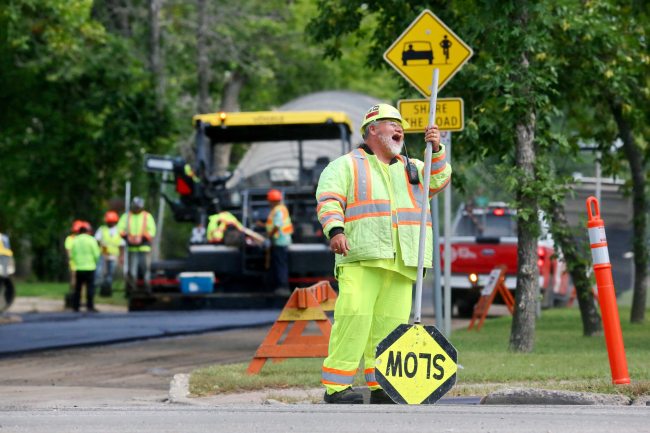 Construction flagger Todd Bone shares a laugh with a co-worker while on the job at the corner of 18th Street and Louise Avenue in Brandon on Tuesday. Bone is part of a construction crew that is in the process of repaving Louise Avenue this week. (Matt Goerzen/The Brandon Sun)