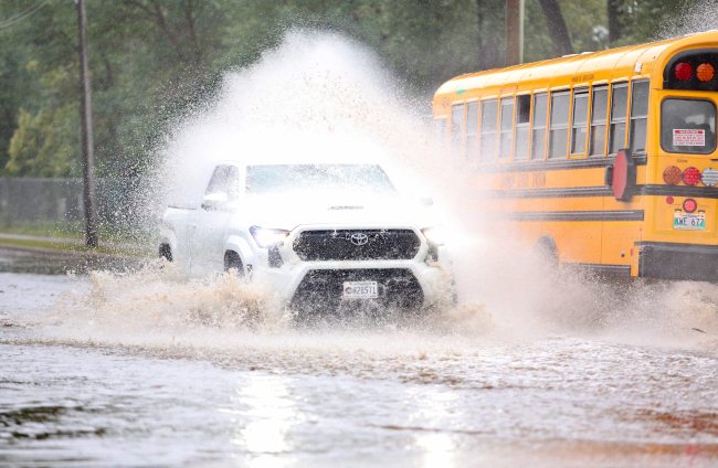 A school bus douses a passing truck with rainwater at a flooded intersection on 13th Street, just in front of the Brandon Fire Station No. 2 after a morning of rain on Monday. (Matt Goerzen/The Brandon Sun)