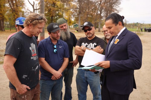 Manitoba Premier Wab Kinew goes over historical articles and photos about the Brandon Residential School with City of Brandon employees at the Brandon Residential School Cemetery site in the former Turtle Crossing Campground along Grand Valley Road on Tuesday. The province announced Tuesday that they had purchased the former campground in partnership with the City of Brandon. The property has long been known to hold the graves of children who attended the nearby Brandon Residential School. The Brandon Residential School opened in 1895 and closed in 1972. The Brandon Residential School Missing Children Investigation, an indigenous-led initiative by SVDN, will conduct an extensive search of the property. The sign acknowledges the significance of the site. 
(Tim Smith/The Brandon Sun)