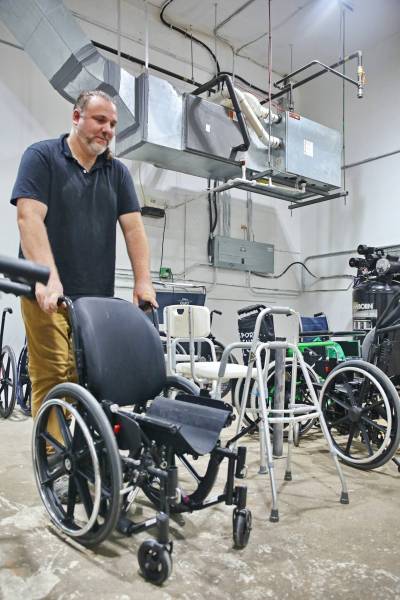Tim Daigle, Creation Nation Makerspace co-ordinator, moves a wheelchair through the room filled with other donated medical equipment that will one day be refurbished by volunteers and resold at a discounted price. (Rylee Gerrard/The Brandon Sun)